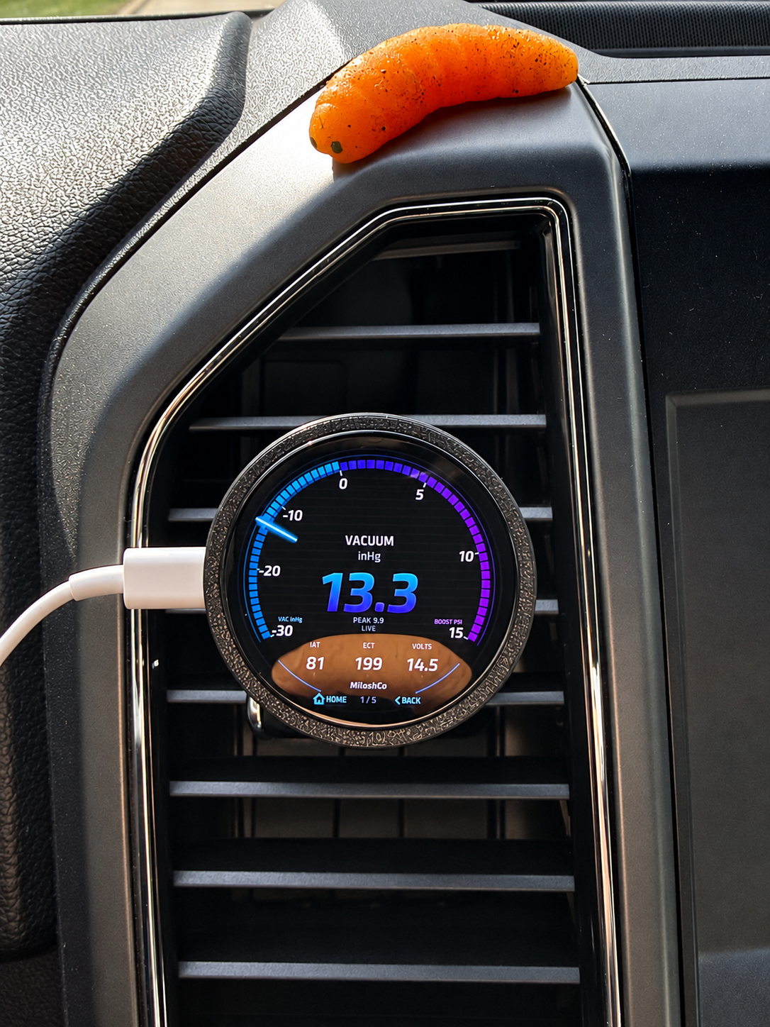 Photo enhanced for clarity: the round MiloshCo gauge in its circular mount on the F-150 air vent, with a USB-C cable at the side.